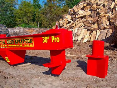 The splitter is mounted on a concrete floor and has a black metal frame with red hydraulic hoses and a control panel.